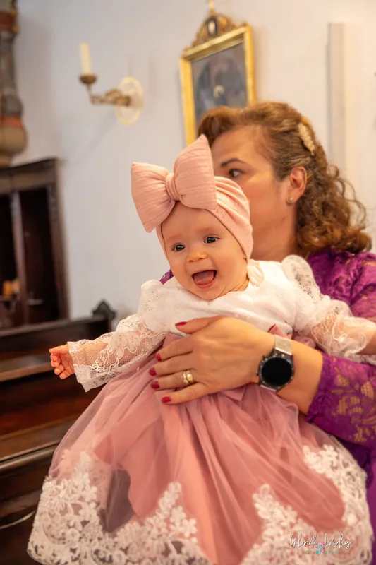 Baby lacht bei der Taufe auf dem Arm einer Angehörigen