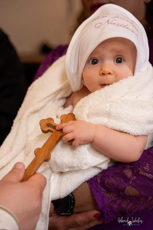 Baby im weißen Tauftuch hält ein kleines Holzkreuz