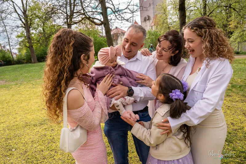 Familie lacht mit dem Täufling nach der Taufe draußen im Grünen