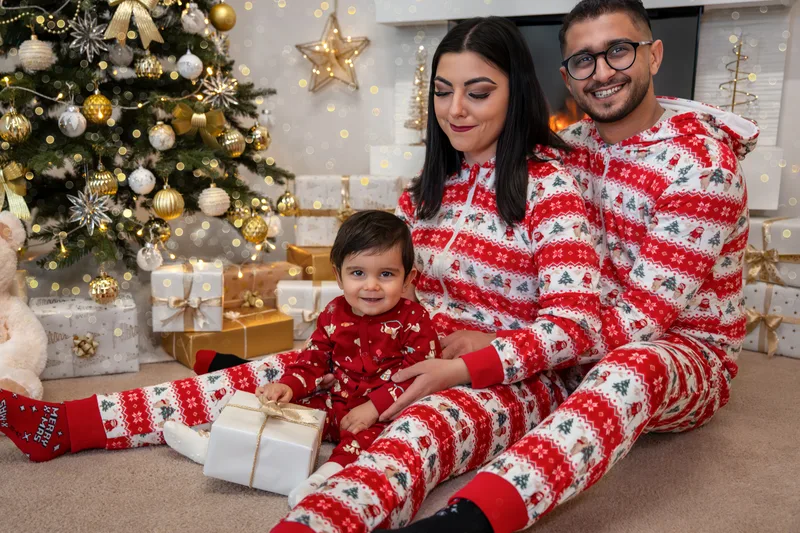 Eltern im rot-weißen Weihnachtspyjama sitzen mit ihrem Sohn vor dem Weihnachtsbaum