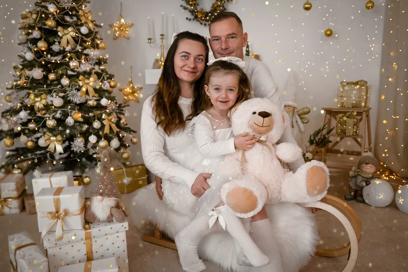Eltern sitzen mit ihrer Tochter und einem großen Teddy vor dem Weihnachtsbaum