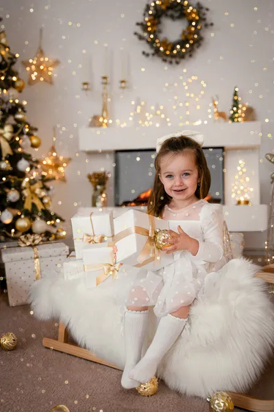 Mädchen im weißen Kleid hält ein Geschenk auf einem Schlitten mit weißem Fell