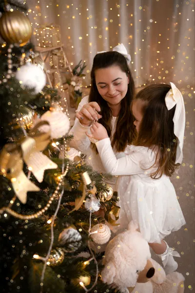 Mama und Tochter betrachten gemeinsam den goldenen Schmuck am Weihnachtsbaum