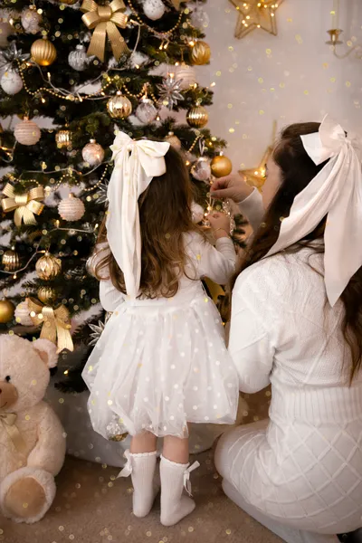 Mama und Tochter mit weißen Haarschleifen betrachten den geschmückten Weihnachtsbaum