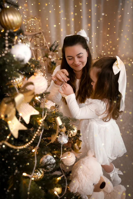 Mama und Tochter betrachten gemeinsam den goldenen Schmuck am Weihnachtsbaum