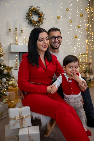 Mama im roten Anzug und Papa mit ihrem Sohn vor dem Kamin