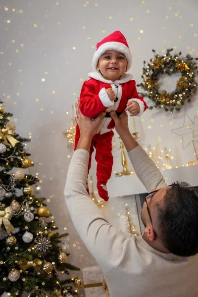 Papa hebt seinen Sohn im Weihnachtsmannkostüm mit roter Mütze hoch