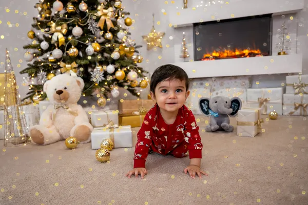Junge im roten Weihnachtspyjama krabbelt vor dem Weihnachtsbaum und dem Kamin