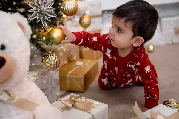 Junge im roten Pyjama greift nach einer goldenen Christbaumkugel