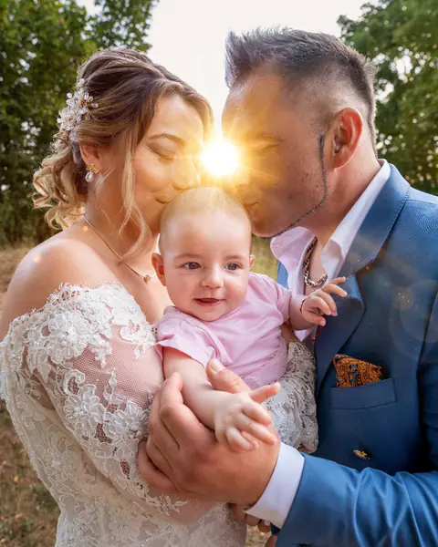 Brautpaar küsst sein Baby, zwischen ihnen die Sonne