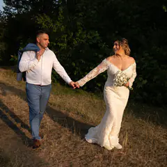 Brautpaar geht Hand in Hand über eine Wiese im Abendlicht