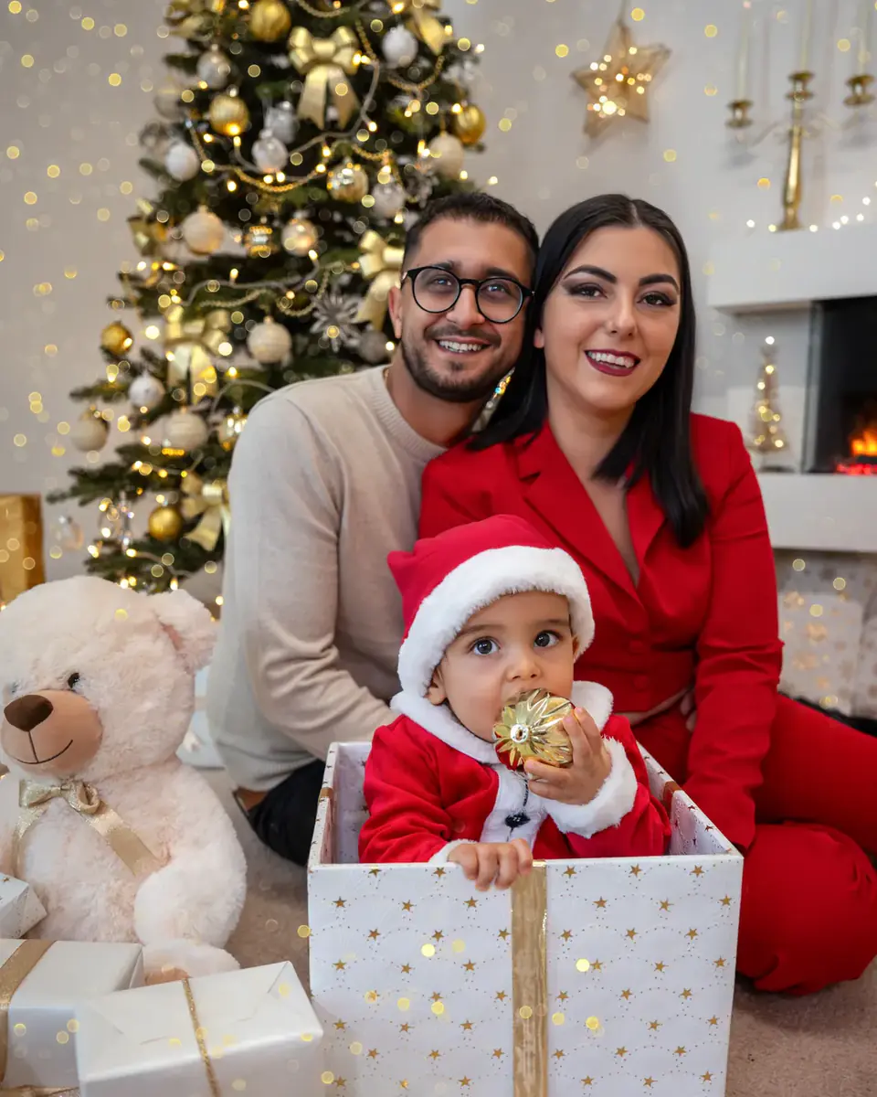 Baby mit Nikolausmütze im Geschenkkarton, die Eltern lachen dahinter
