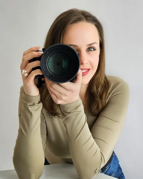 Gabriela Lederhos hält ihre Kamera vor das Gesicht, im olivgrünen Pullover