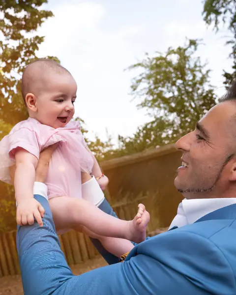 Papa hebt sein lachendes Baby im Gegenlicht in die Luft