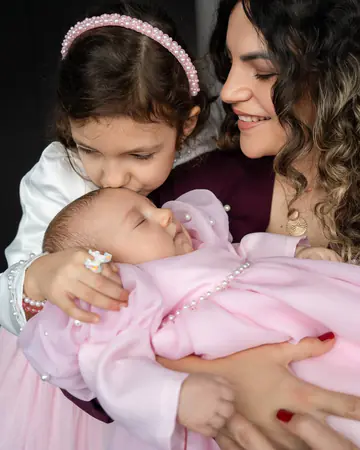 Große Schwester küsst das Baby im rosa Taufkleid