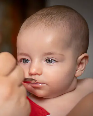 Baby empfängt bei der Taufe die Kommunion vom Löffel